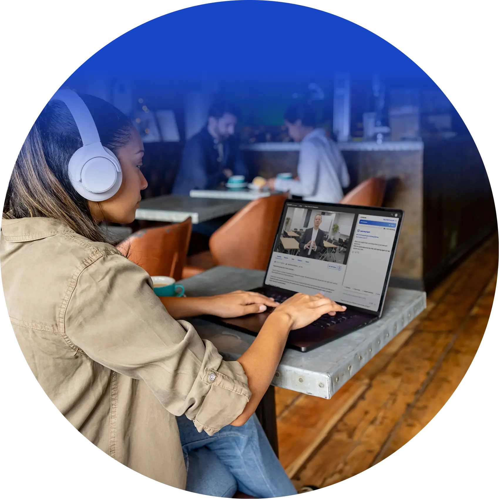 Woman wearing headphones studying an online course on her laptop at a cafe table.