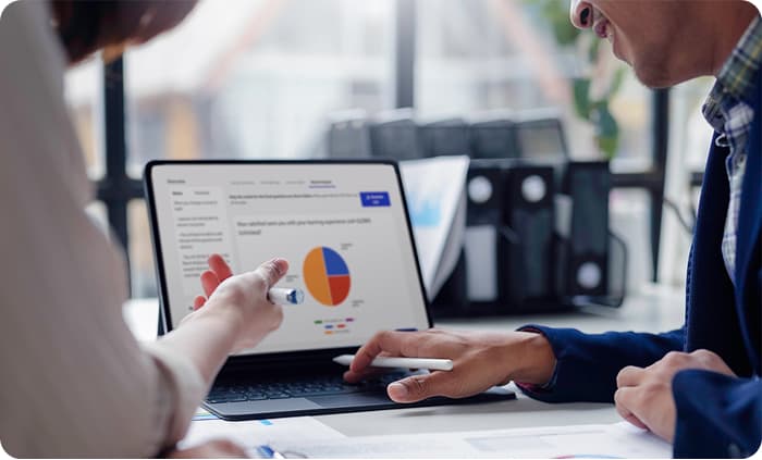 Two colleagues pointing at a pie chart report on a laptop screen during a training review.