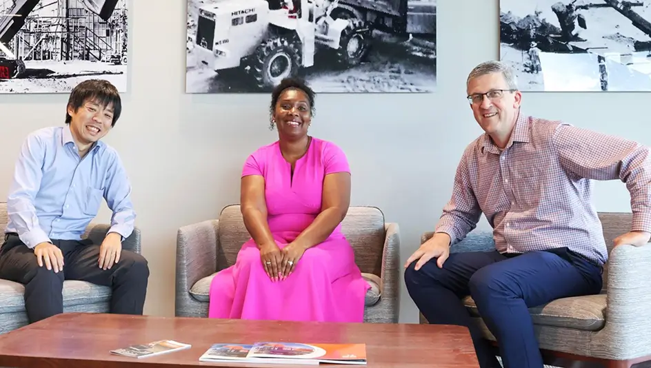 Three members of Hitachi Construction Machinery Americas sitting in armchairs and smiling.